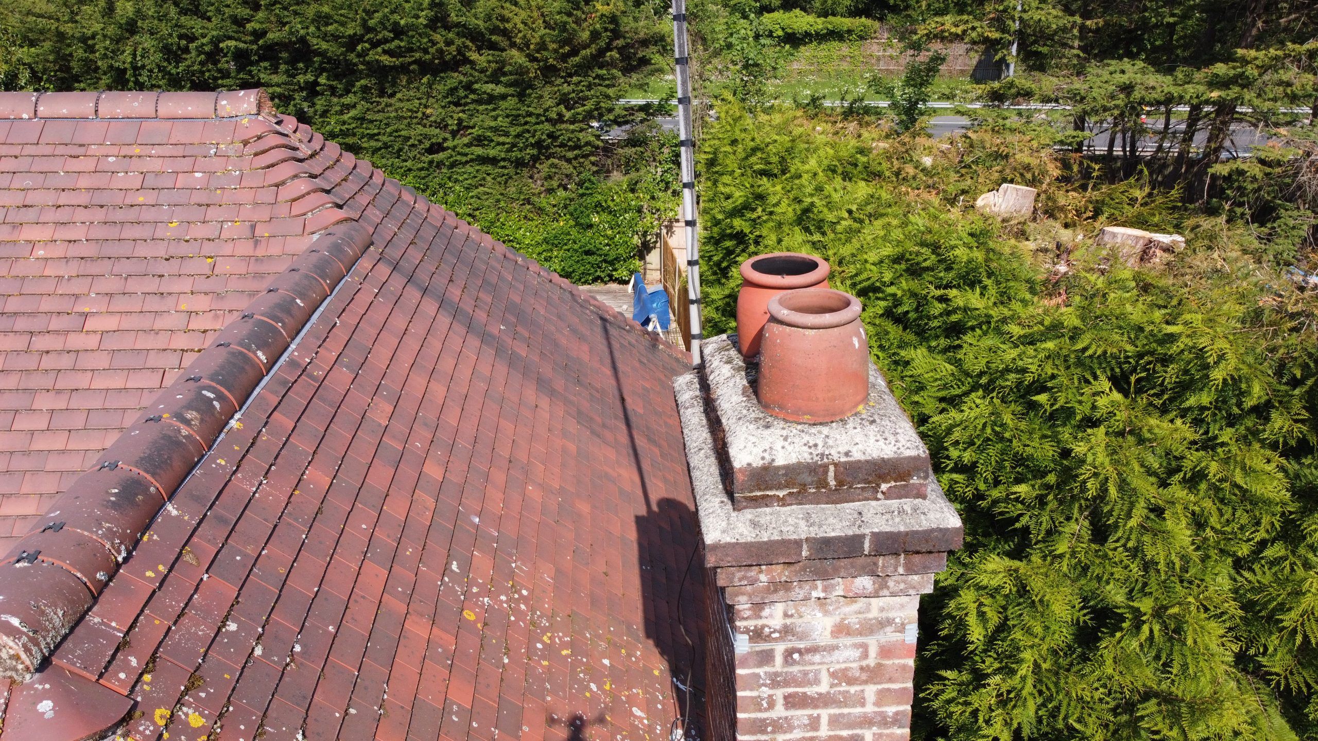 Surveyor with safety harness inspecting ridge tiles and flashings on a British residential roof